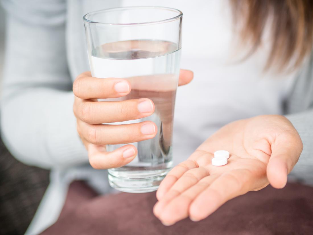woman holding tablets and glass of water