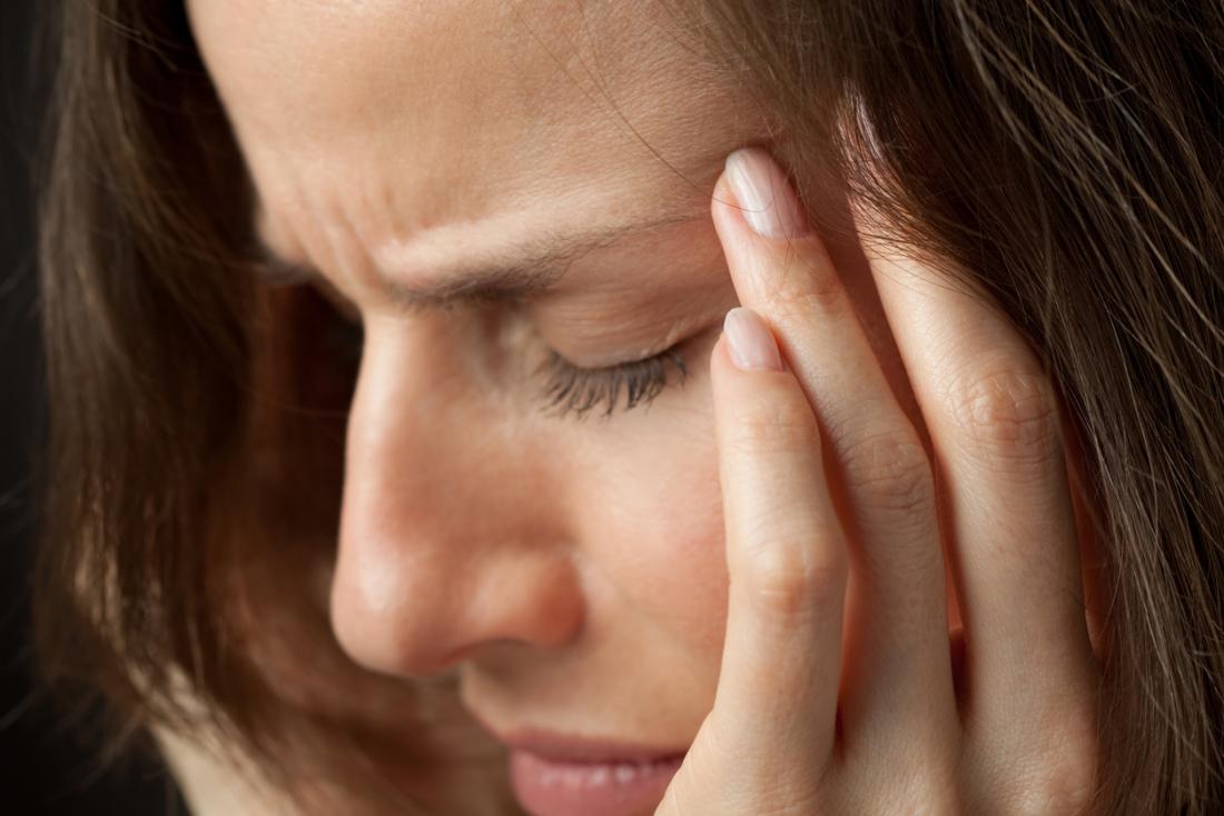 woman holding the side of her temple in pain because of a basilar migraine<!--mce:protected %0A-->