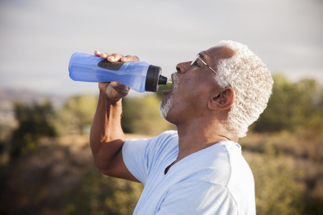 a man drinking water whilst outside on a sunny day.
