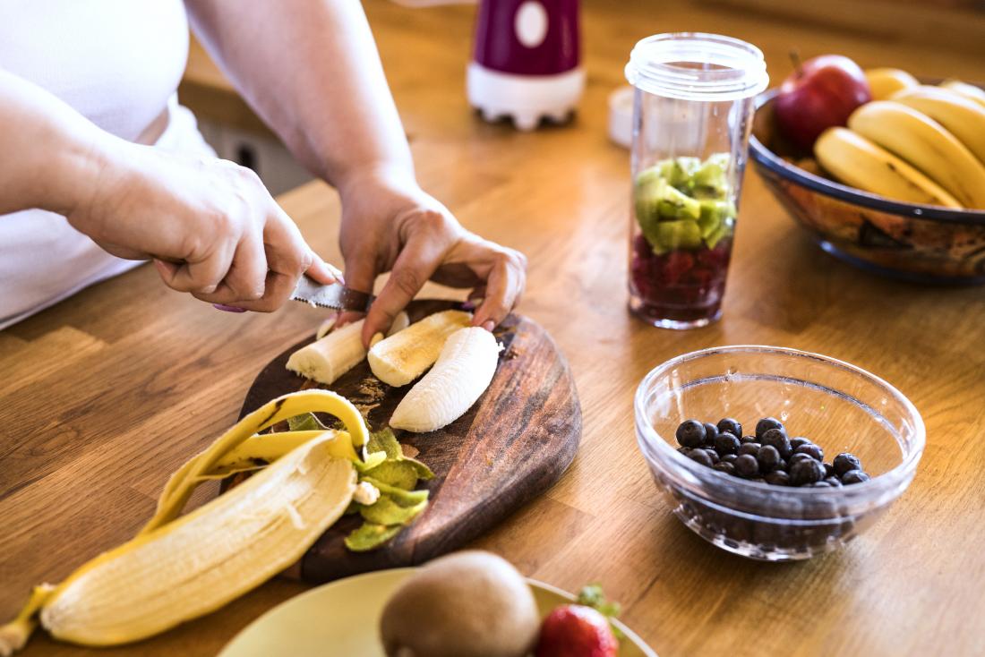 person chopping or cutting fruits for smoothie or juice including banana kiwi and blueberries