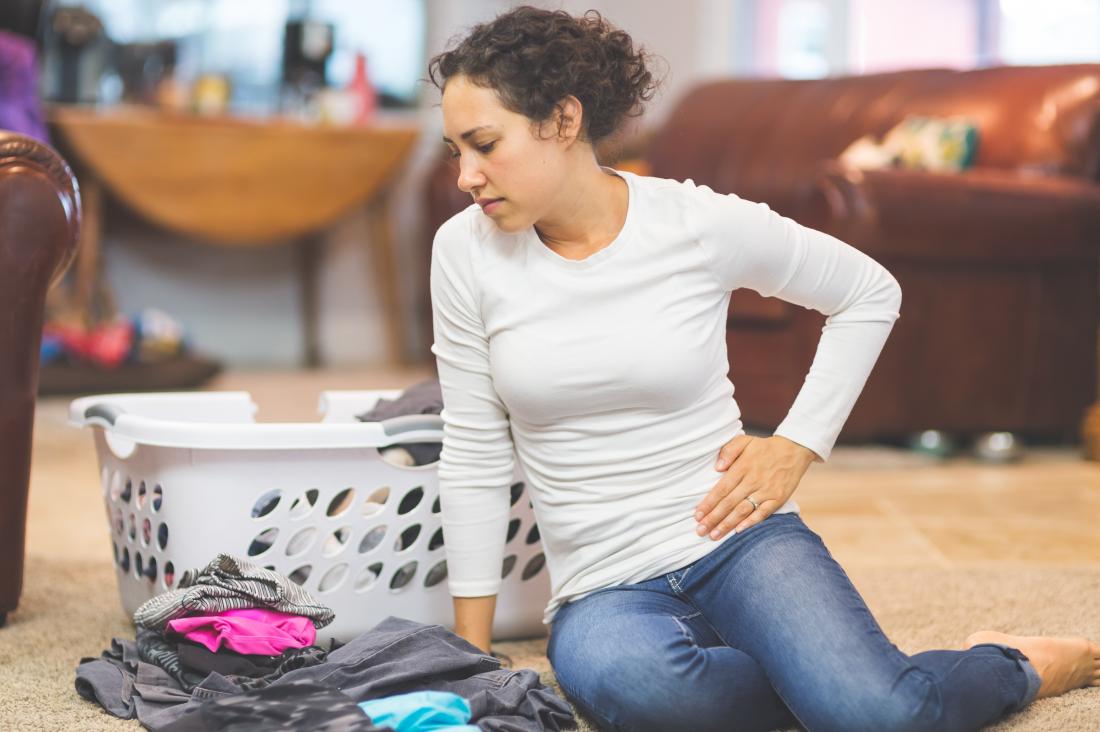 woman sitting on the floor with washing holding side in pain