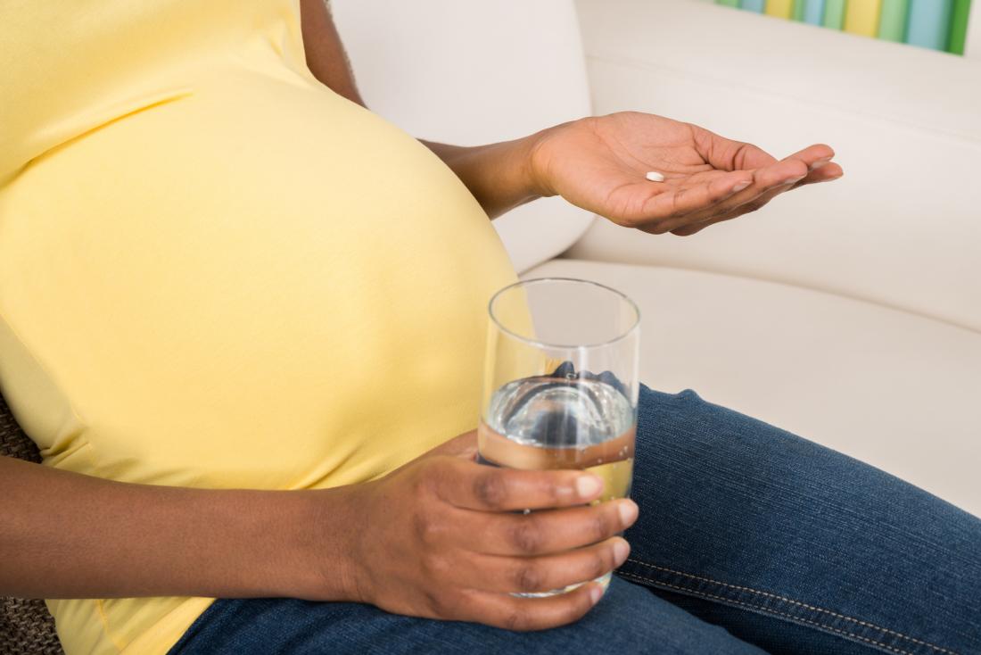 a pregnant woman taking a supplement with a glass of water. 