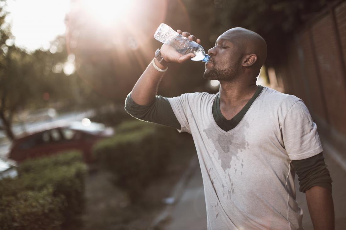 a man experiencing painful respiration and excessive sweating drinks from a water bottle outside