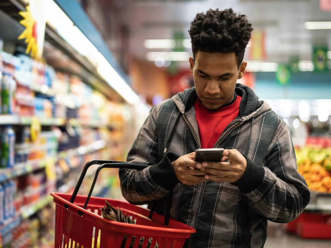 a man in a supermarket looking at information on Keto vs atkins on his phone.