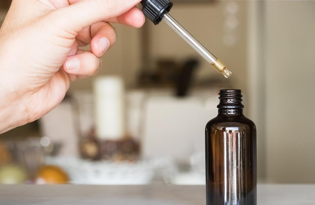 person using dropper of essential oil from glass bottle