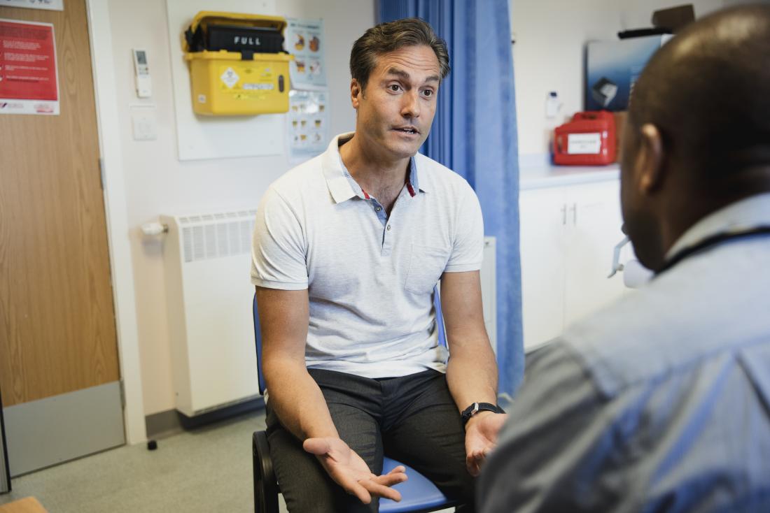 man discussing health problem in doctor s office with doctor in foreground