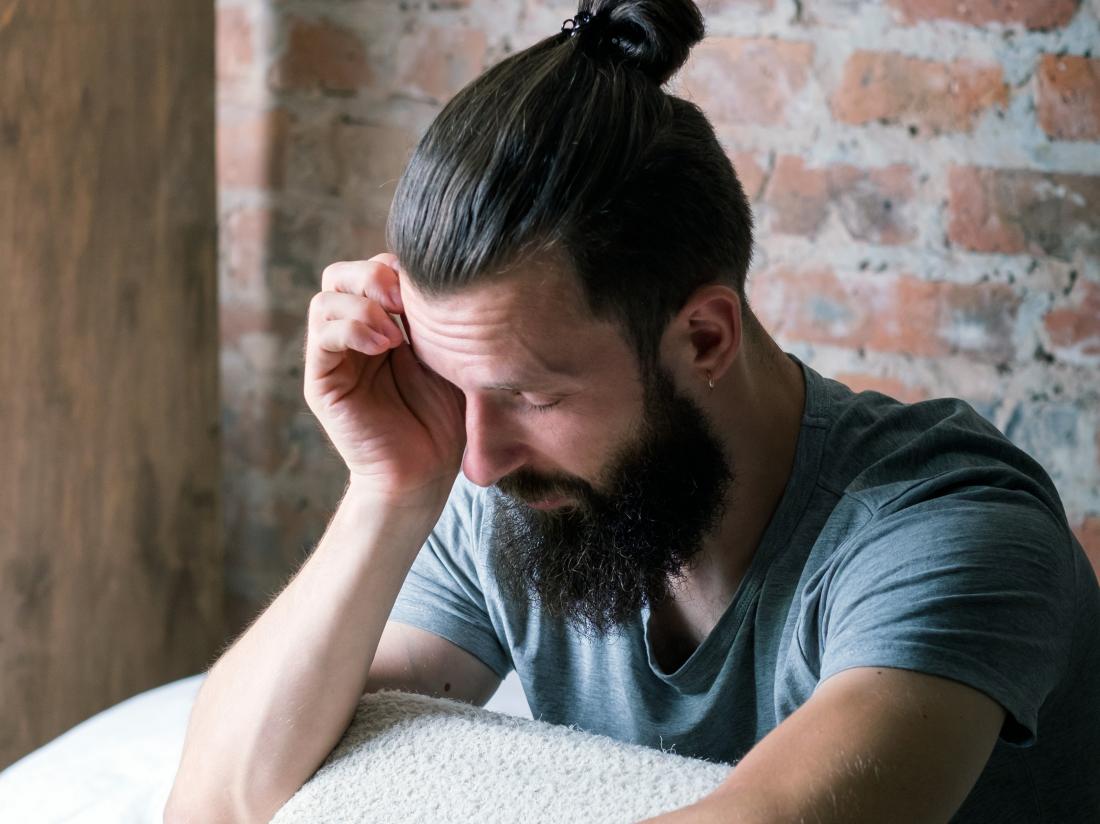 a man with a manbun experiencing drowsiness and a headache.