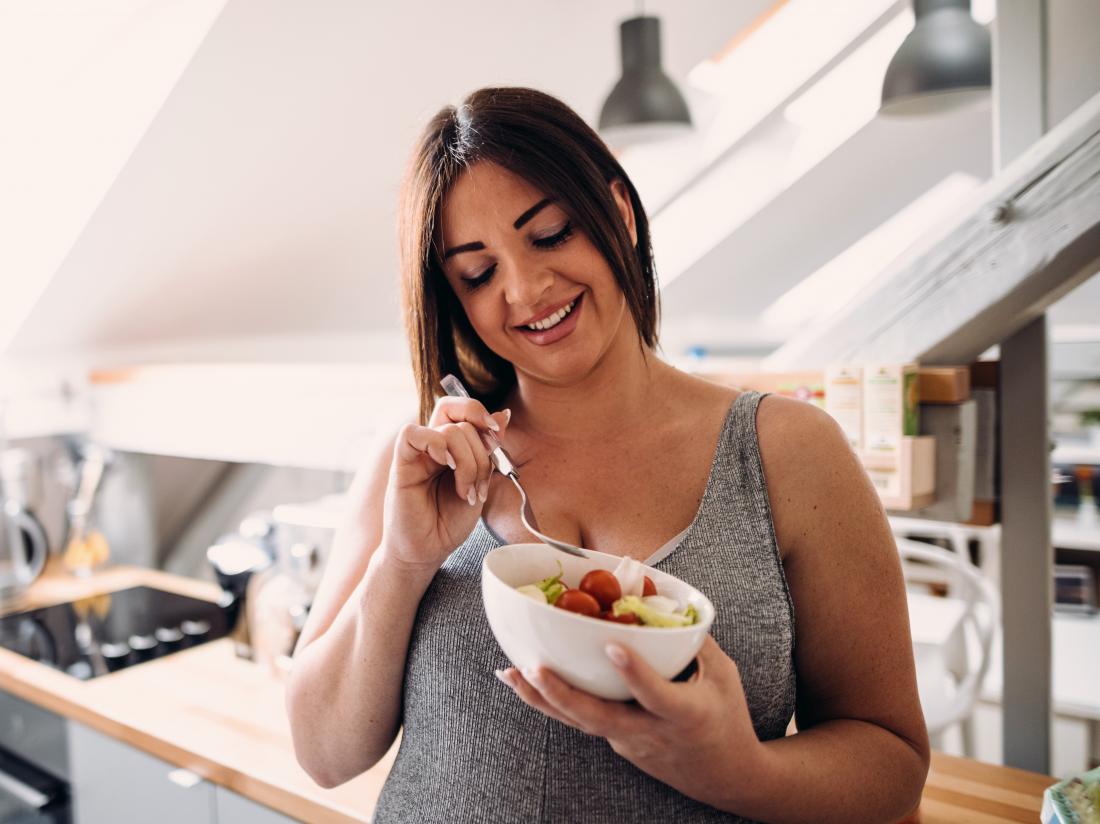 a happy woman eating fruit in a bowl in her kitchen 
