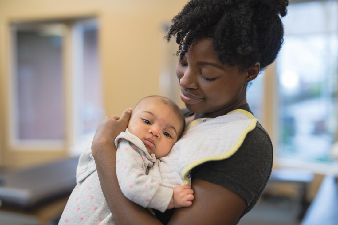 a mother holds her infant while talking her to see a doctor.