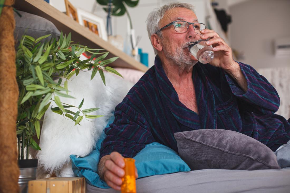 senior man in bed taking prescription medication statin pills and drinking water