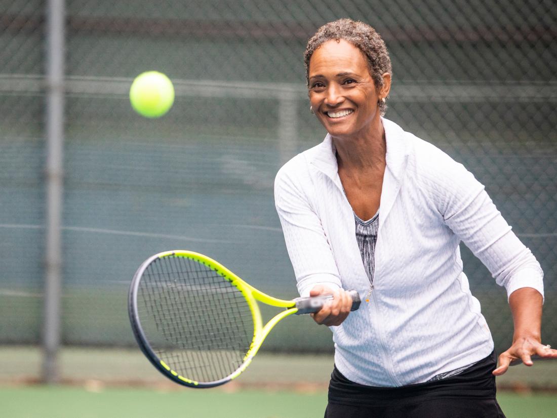 a senior woman playing tennis with a smile