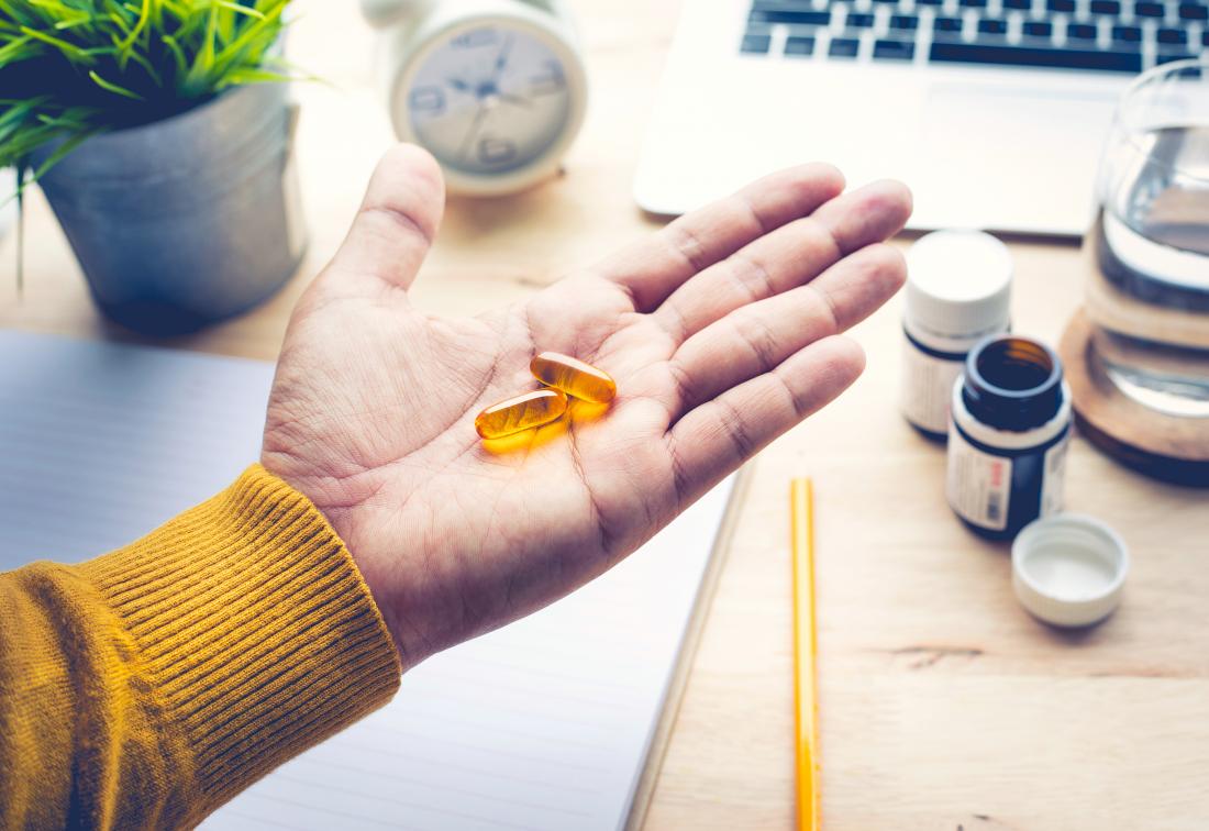 person at desk holding omega 3 supplements in palm