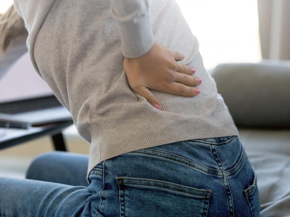 a woman holding her back because of kidney pain and wondering how long it will take to pass