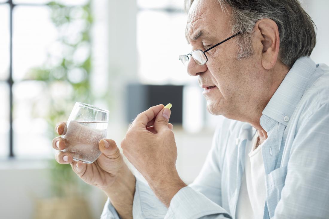 senior man taking supplements with glass of water