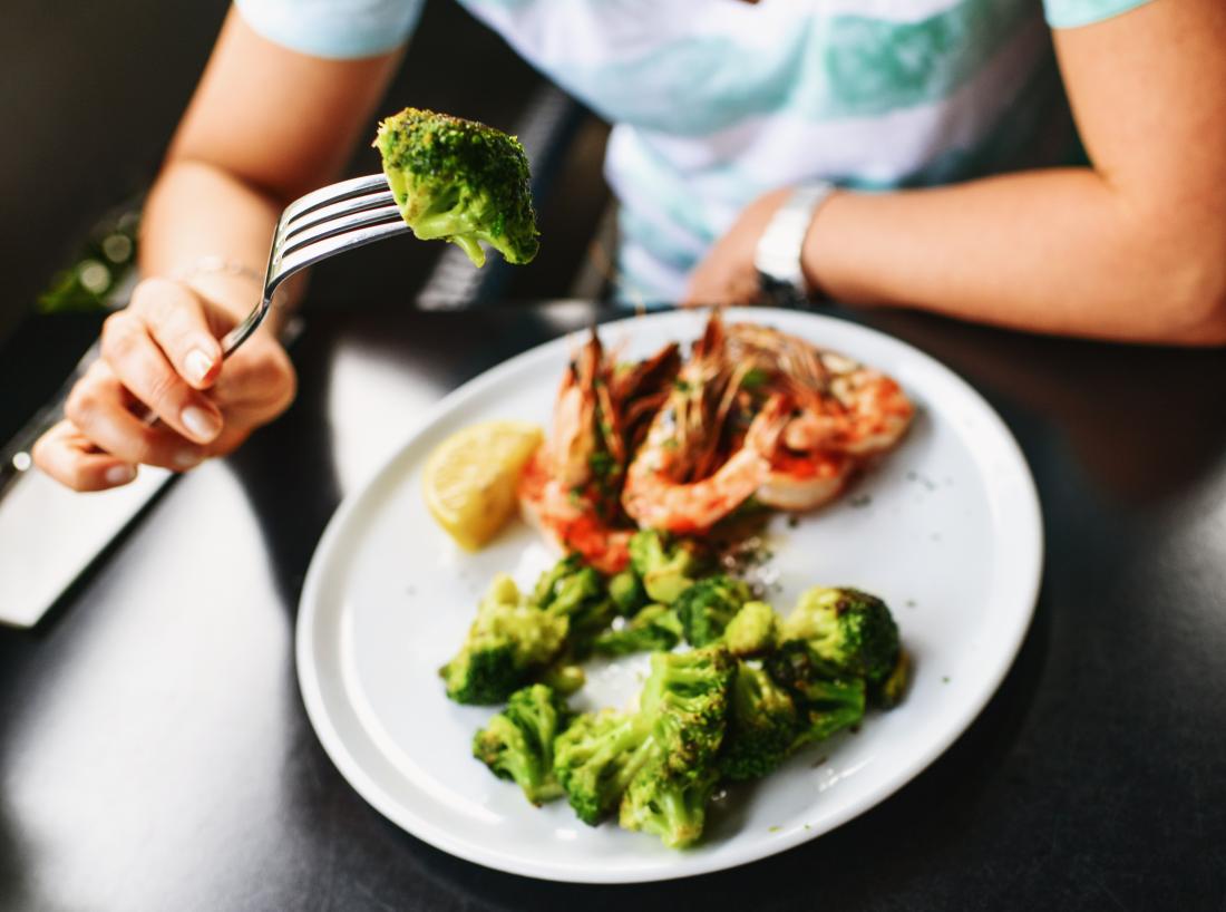 a person eating broccoli and prawns as part of a candida diet