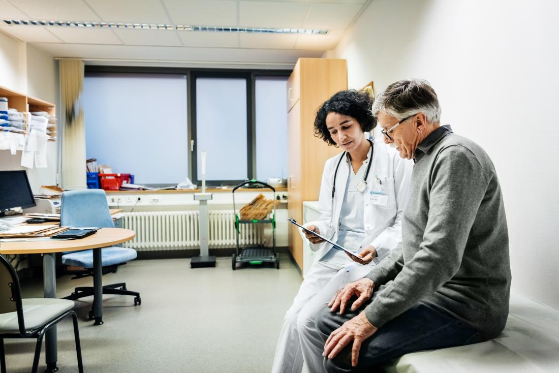 senior adult male speaking to doctor in office looking at clipboard