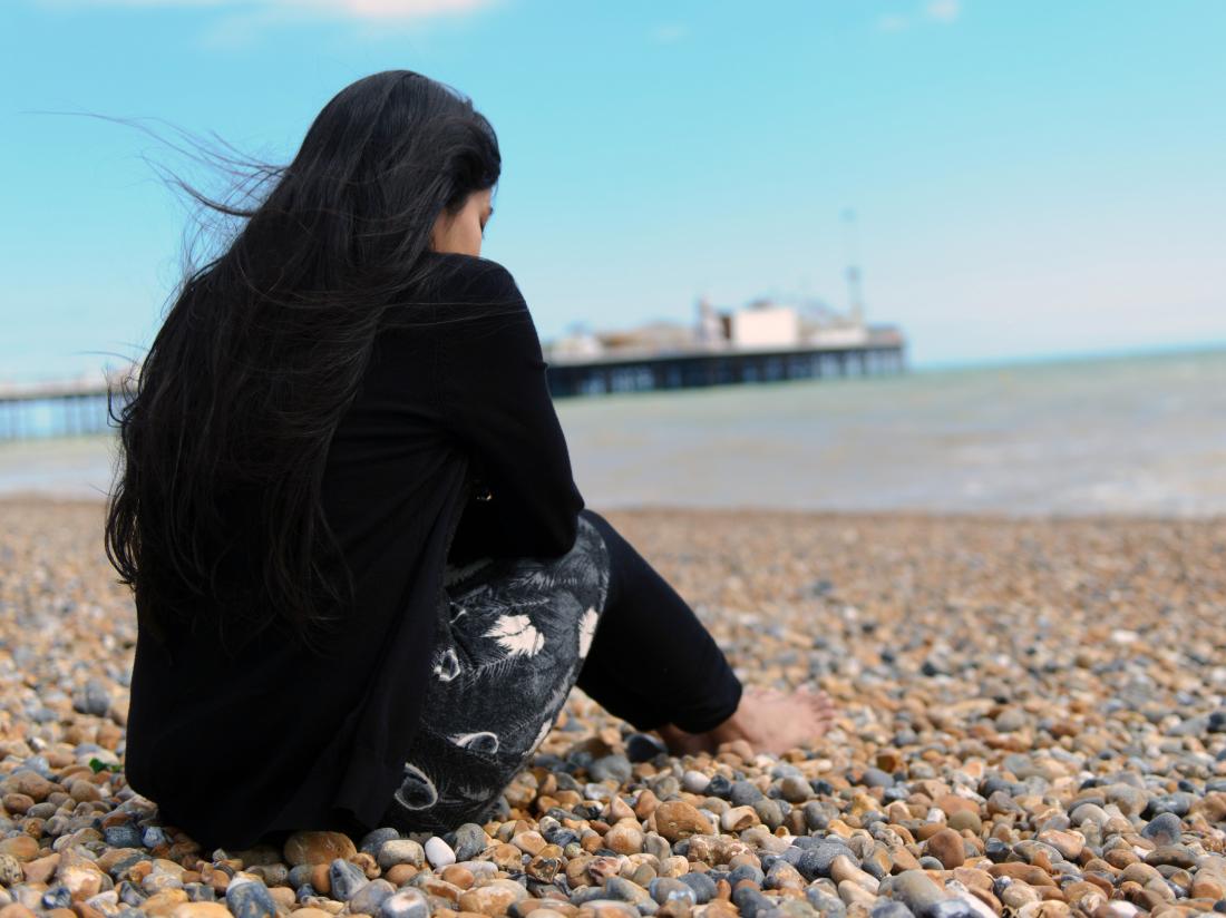 a woman looking depressed sat on a beach.