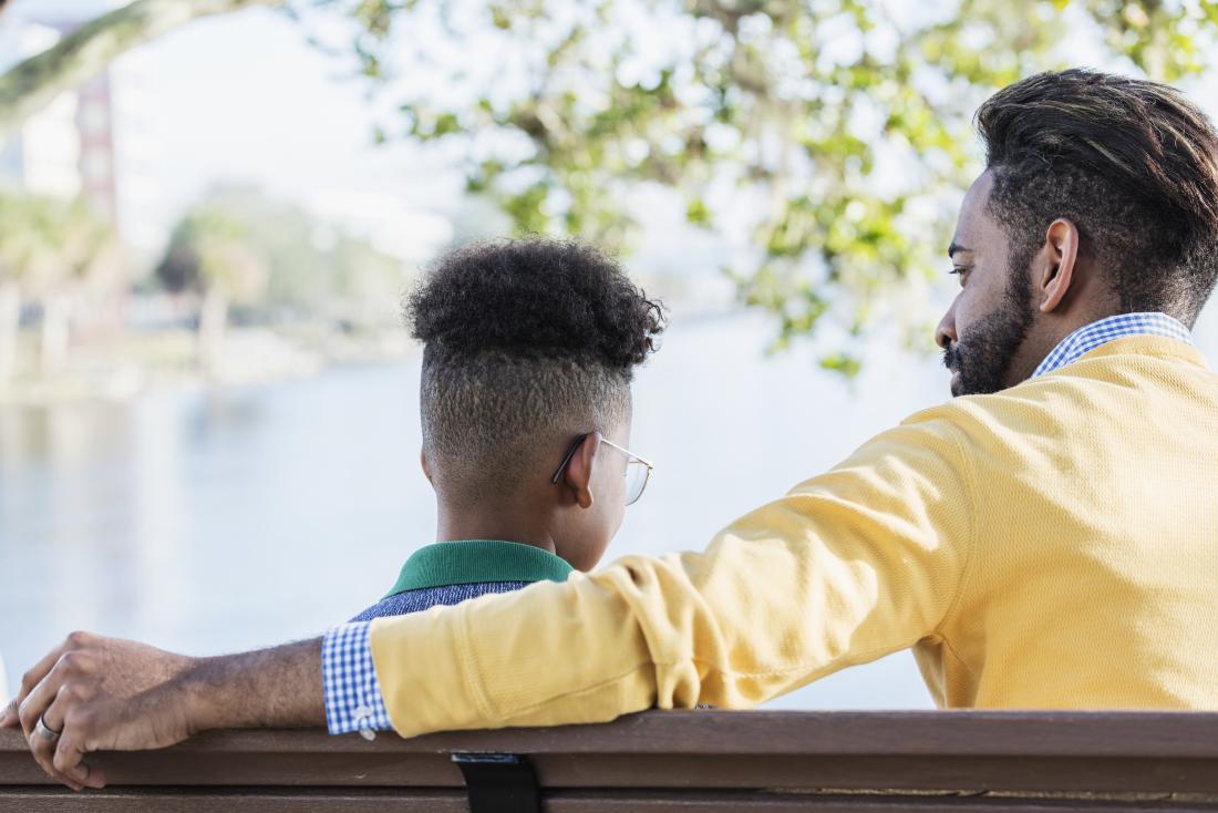 a father and son sat on a bench facing a body of water